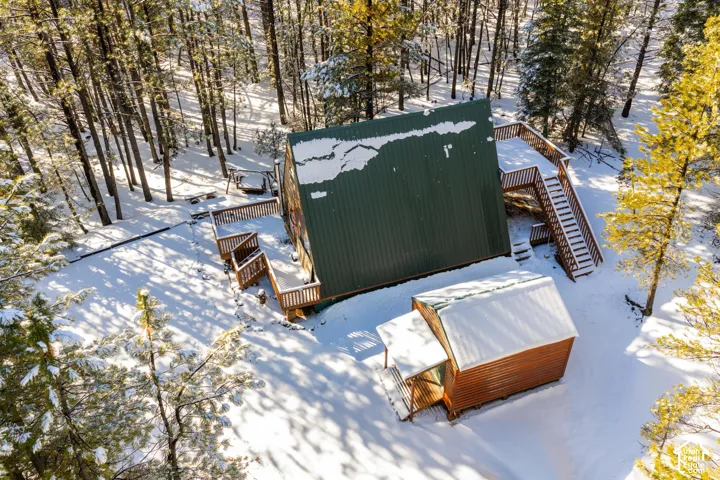 A-frame residence featuring a green metal roof, multiple levels of exterior wooden decking, an attached staircase, and a separate wood-sided outbuilding situated on a forested lot