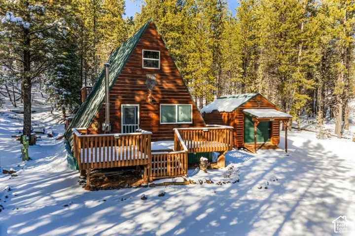 A-frame cabin exterior featuring horizontal wood siding, a standing seam metal roof, and an expansive elevated wood deck
