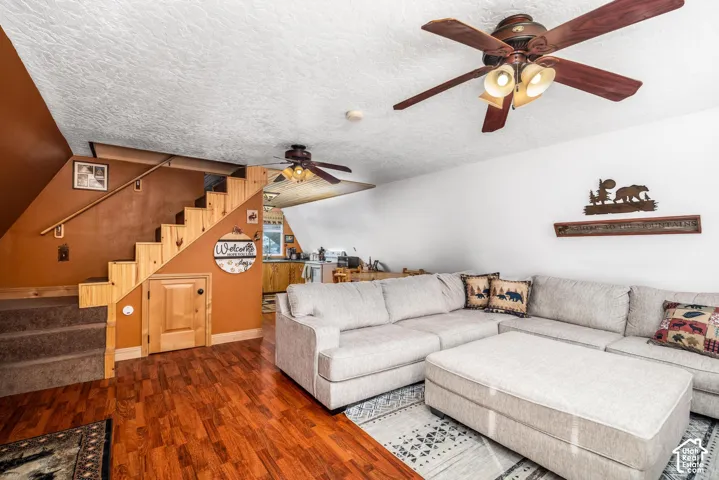 Living area featuring wood-finish flooring, wood-toned staircase with integrated storage, and two ceiling fans with integrated light fixtures