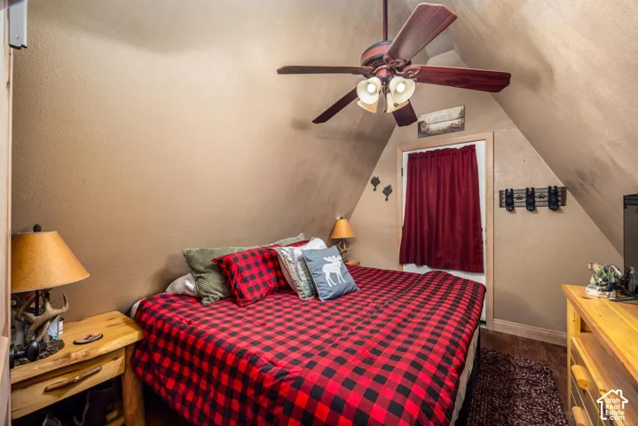 Sloped ceilings featuring a centrally mounted ceiling fan with integrated lighting and wood-finish flooring