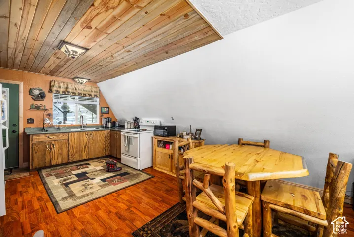 Kitchen featuring wood-finish cabinetry, a sloped ceiling with wood-plank cladding, wood-finish flooring, and a window above the sink