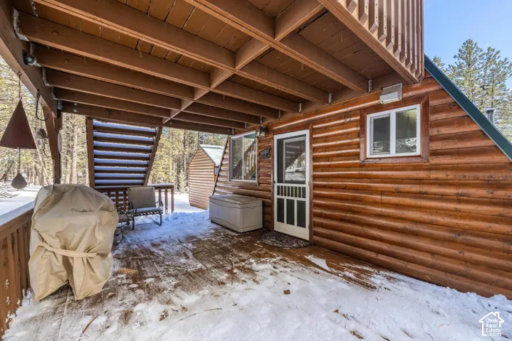 Covered wood deck featuring log siding, exposed timber ceiling beams, and integrated staircase