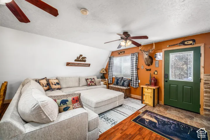 Living area featuring wood-finish flooring, a ceiling fan with integrated lighting, a solid green exterior door with an inset window, and a window with a sloped wall detail