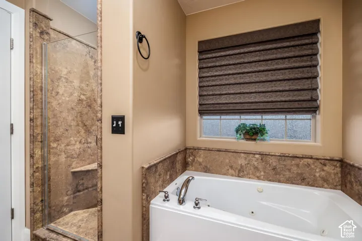 Jetted soaking tub with chrome hardware, glass-enclosed shower with built-in bench, and tile surround