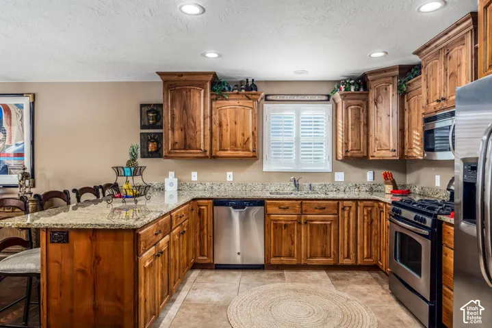 Kitchen featuring custom stained-wood cabinetry, stone countertops, stainless steel appliances, tile flooring, and recessed lighting