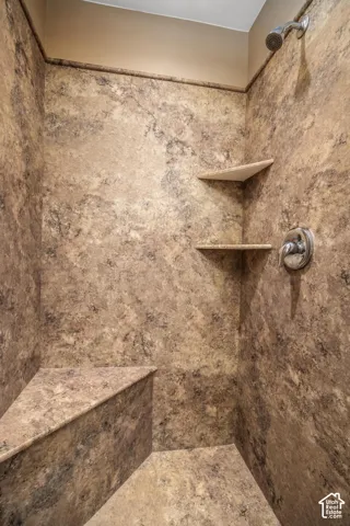 Shower stall featuring full-height composite surrounds with a stone-finish pattern, built-in corner bench, dual integrated shelving, and a chrome single-handle pressure balance valve