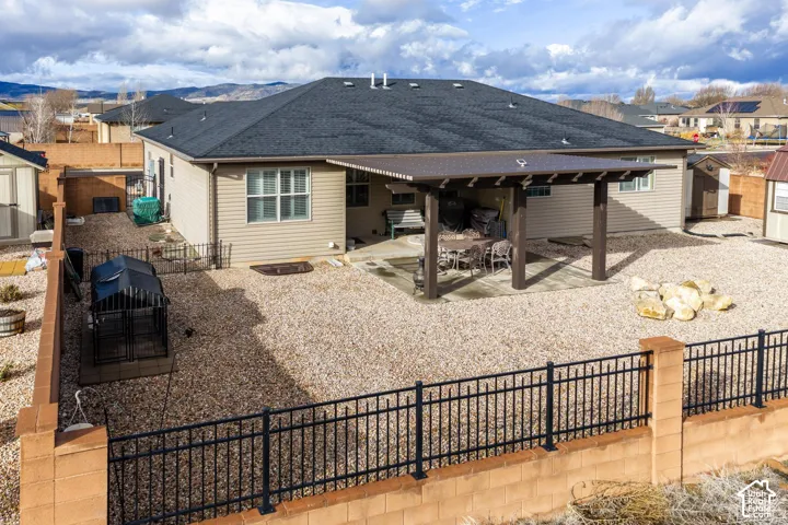 Rear exterior featuring a covered patio, decorative rock landscaping, metal perimeter fencing, and concrete masonry unit walls