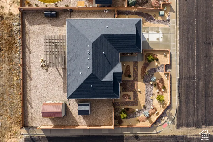 Aerial view of corner lot property featuring a hip roof, integrated pergola, xeriscaped landscaping with stone accents, and perimeter fencing