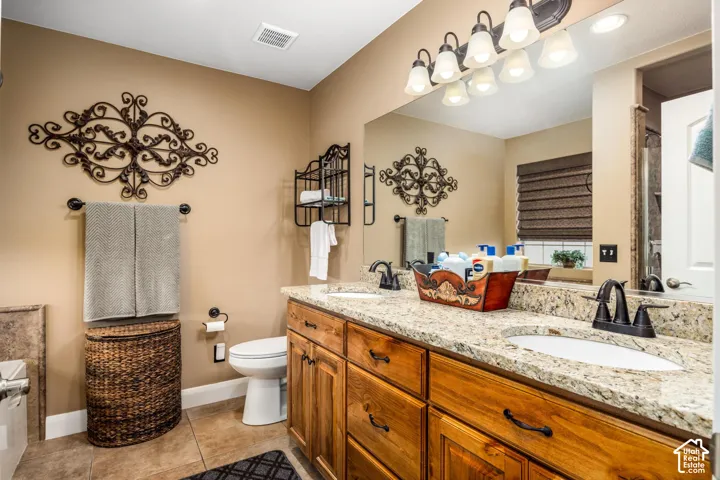 Dual-sink vanity with stone-finish countertop, dark metal hardware, wood-finish cabinetry, and oversized wall-to-wall mirror