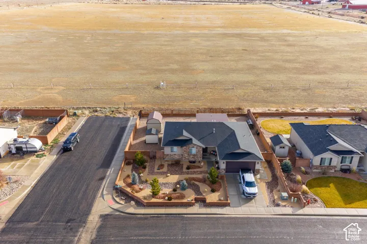 Aerial perspective of a corner-lot property featuring a stone and siding exterior, multi-pitched roofline, xeriscaped front yard, and two detached storage structures