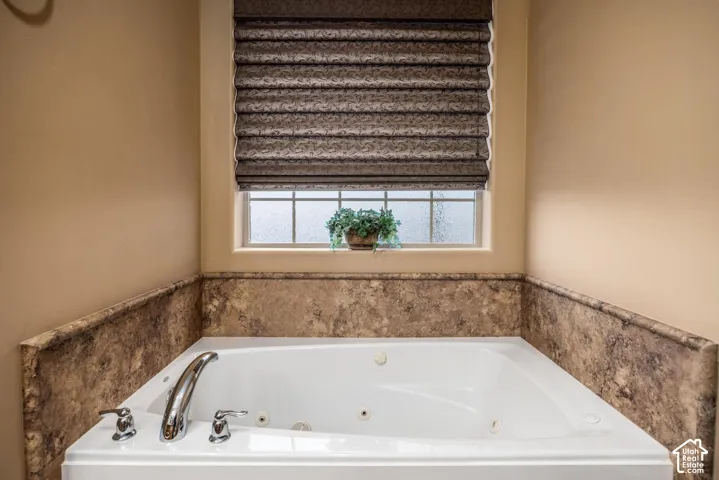 Built-in jetted tub featuring stone-finish surround and polished chrome deck-mounted faucet hardware set below a window with a built-in shade