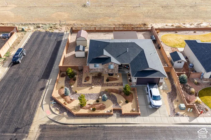 Single-story residence featuring a stone-accented facade, asphalt shingle roof, two detached storage structures, and a xeriscaped front yard enclosed by a perimeter wall