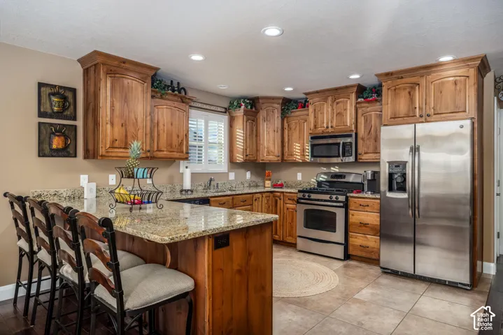 Kitchen featuring knotty wood cabinetry, stone countertops, stainless steel appliances, a center island with bar seating, and tile flooring
