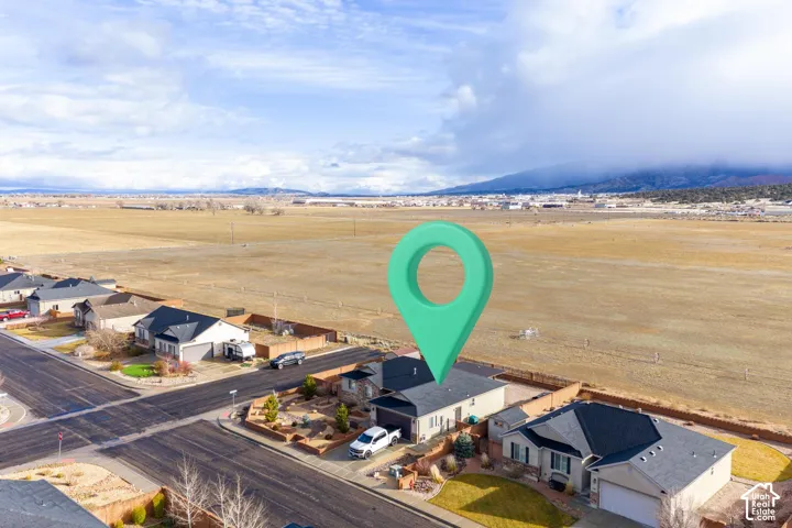 Aerial view of a residential lot featuring an asphalt driveway, a detached garage, and a fenced perimeter, set against a expansive mountain backdrop