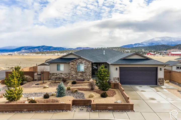Single-story residence featuring stone veneer siding, an attached two-car garage, concrete driveway, xeriscaped front yard with masonry retaining walls, and mountain backdrop