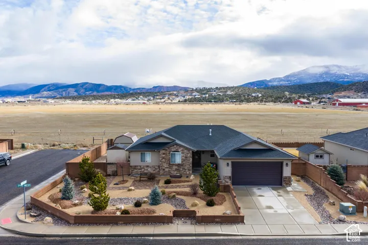 Single-story residence featuring stone veneer siding, an attached two-car garage, concrete driveway, decorative rock landscaping, and surrounding mountain scenery