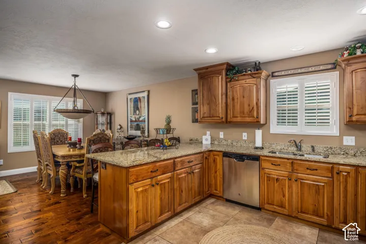 Kitchen featuring stained wood cabinetry, stone countertops, stainless steel dishwasher, recessed lighting, and plantation shutters