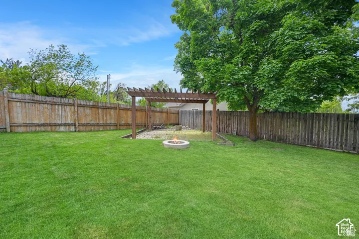 Backyard featuring a grass lawn, a wood-framed pergola, a circular stone fire pit, and privacy fencing