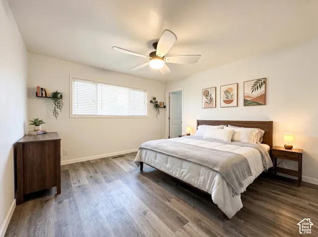 Neutral-toned interior space featuring wood-finish flooring, a multi-blade ceiling fan with integrated lighting, and a wide window with horizontal blinds