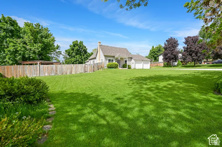 Expansive lawn with mature landscaping, wood-paneled privacy fencing, two-car garage, and pergola hardscaping
