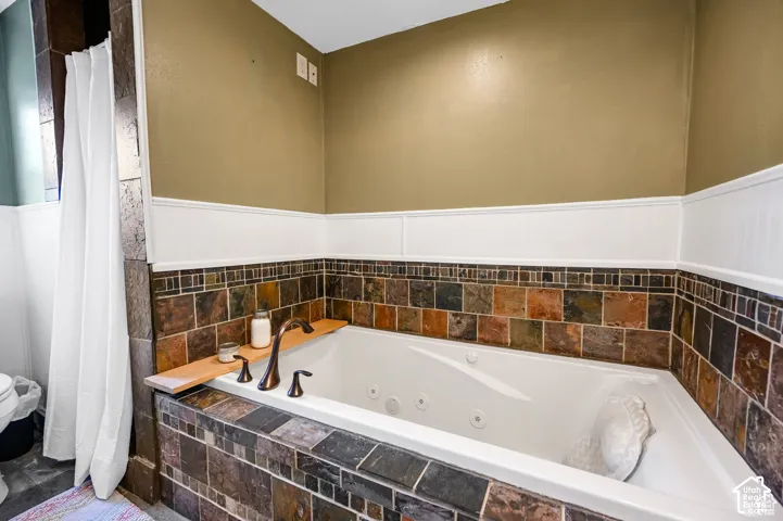 Jetted soaking tub with an integrated wooden deck, framed by multi-tonal stone tile surround and white wainscoting