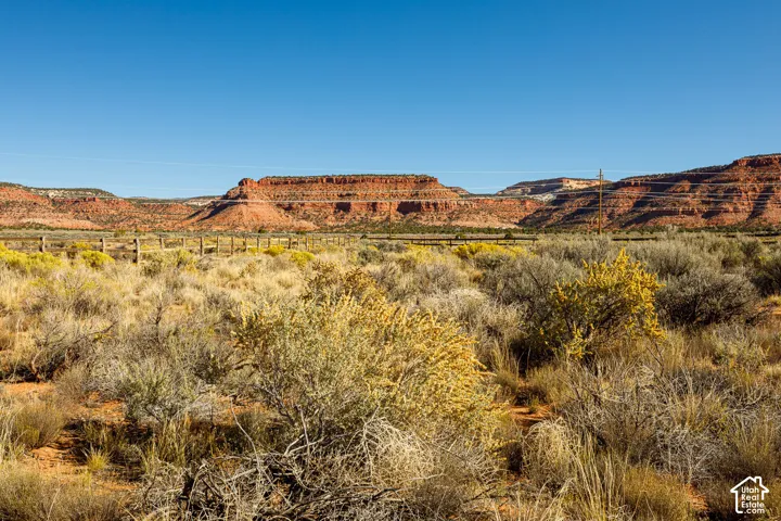 Expansive desert landscape featuring native brush, a post-and-rail fence, and prominent red rock mesa formations