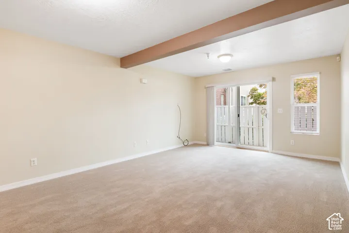 Neutral-toned carpeted flooring, exposed wood-finish beam, sliding glass door, and single-pane window