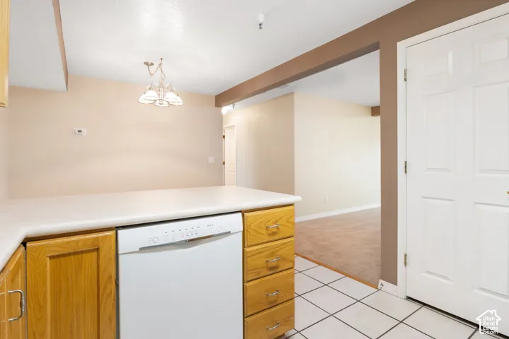 Kitchen featuring wood cabinetry, a solid-surface countertop, an integrated dishwasher, white tiled flooring, and a multi-light pendant fixture