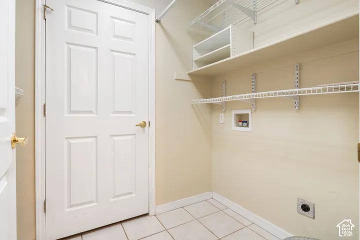 Utility area featuring ceramic tile flooring, a six-panel door, built-in open shelving, wire rack storage, and dedicated water and electrical hookups