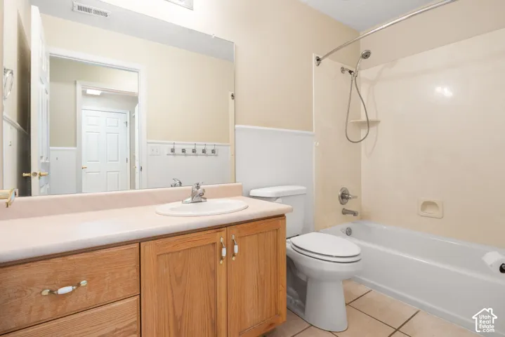 Bathroom featuring wood-finish cabinetry, a white vanity top with an integrated sink, beadboard wainscoting, and a bathtub-shower combination with a surround