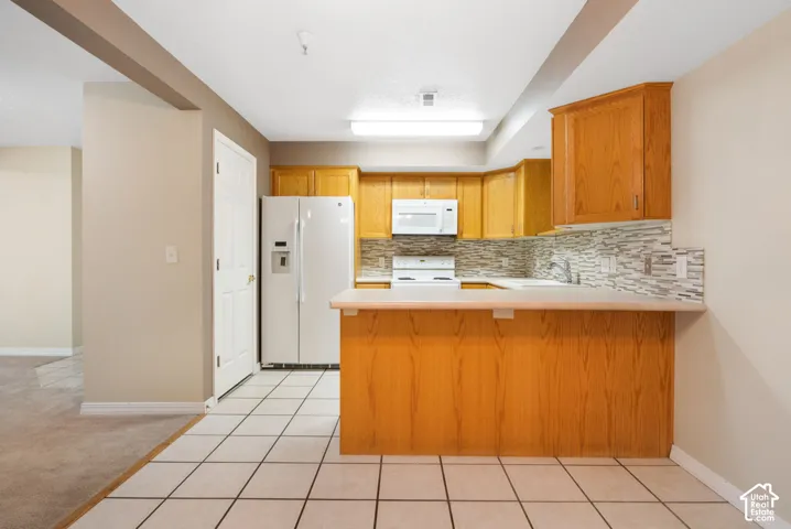 Kitchen featuring natural wood-finish cabinetry, tile flooring, a peninsula breakfast bar, and a stone-patterned tile backsplash