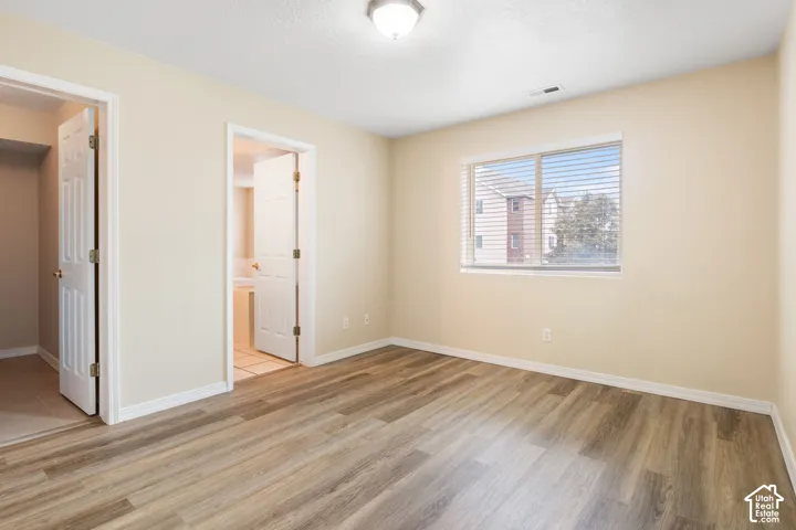 Neutral-toned room featuring wood-finish flooring, two white panel doors, and a window with horizontal blinds