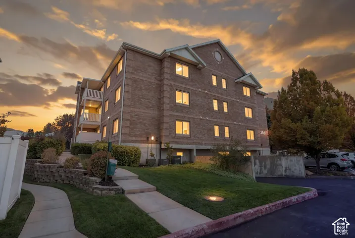 Multi-story brick exterior featuring stacked balconies, concrete block retaining walls, asphalt paved parking, and concrete walkways