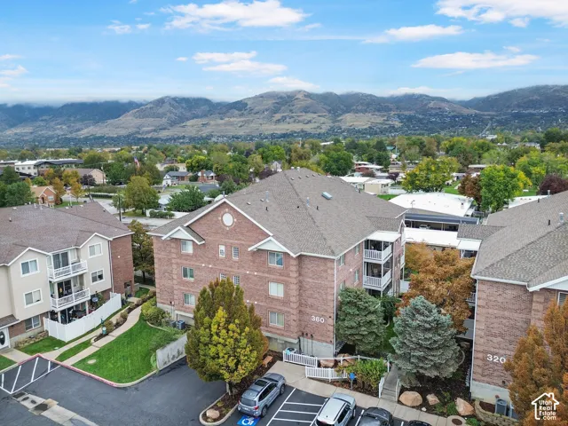Brick exterior multi-story residential building featuring gabled rooflines, private balconies, and asphalt-paved surface parking, set against a backdrop of mountain scenery