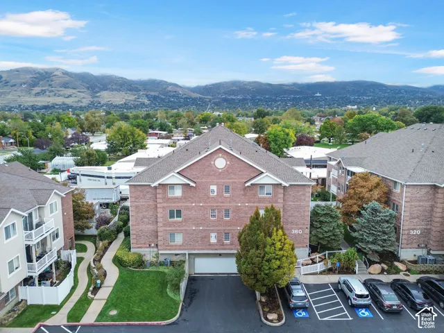 Multi-story brick exterior building featuring a paved driveway, designated parking stalls, manicured lawn areas, and a mountain backdrop
