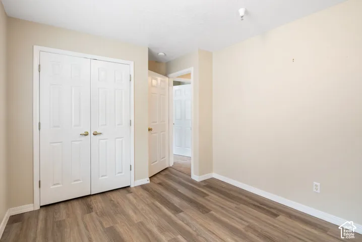 Neutral-toned interior space featuring wood-finish flooring, double-door closet with brass-finish hardware, and recessed ceiling lighting