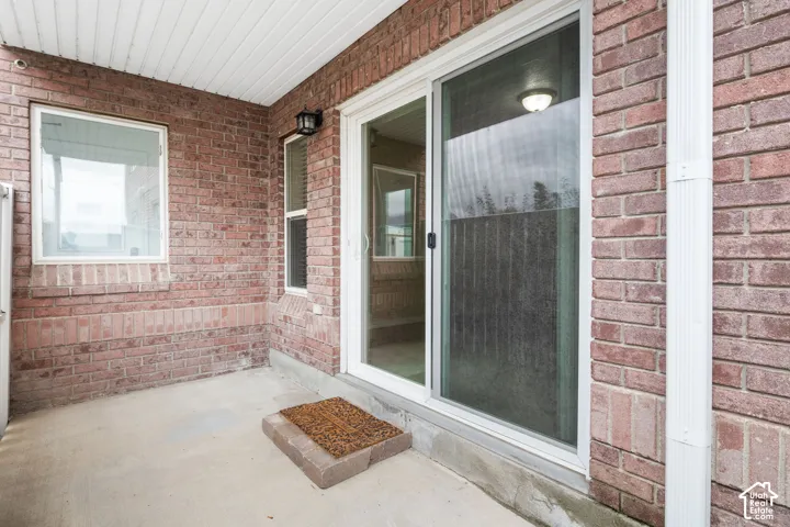 Covered concrete patio featuring brick exterior walls, a sliding glass door, and a wall-mounted exterior light fixture