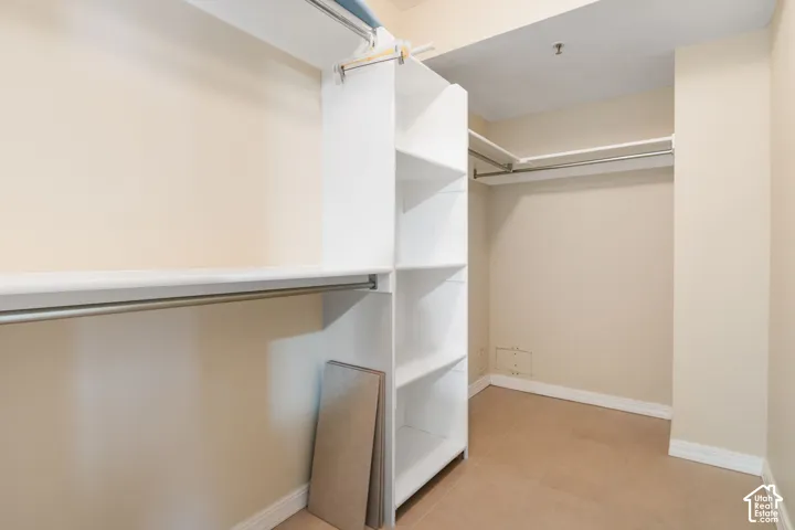 Walk-in closet featuring white built-in shelving, integrated hanging rods, and tile flooring