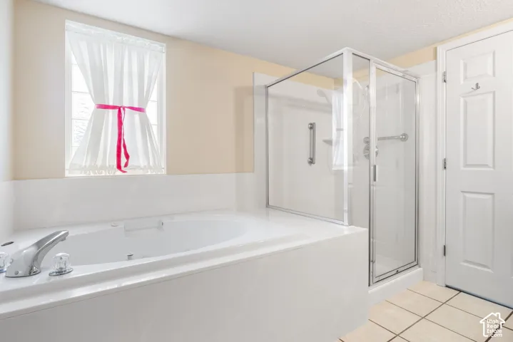 Built-in soaking tub with chrome faucet, separate glass-enclosed shower, tile flooring, and six-panel interior door