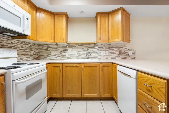 Kitchen featuring natural wood cabinetry, mosaic tile backsplash, solid-surface countertops, and white appliances