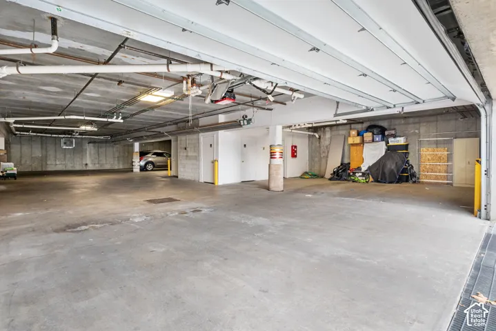 Expansive covered parking area featuring a smooth concrete floor, exposed structural ceiling, integrated overhead lighting, and protective yellow bollards