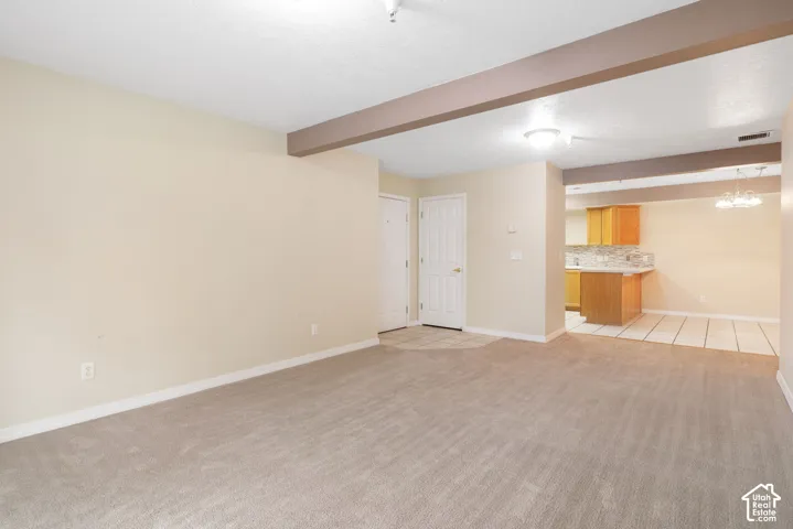Open interior space featuring exposed ceiling beams, neutral carpeting, and tile flooring