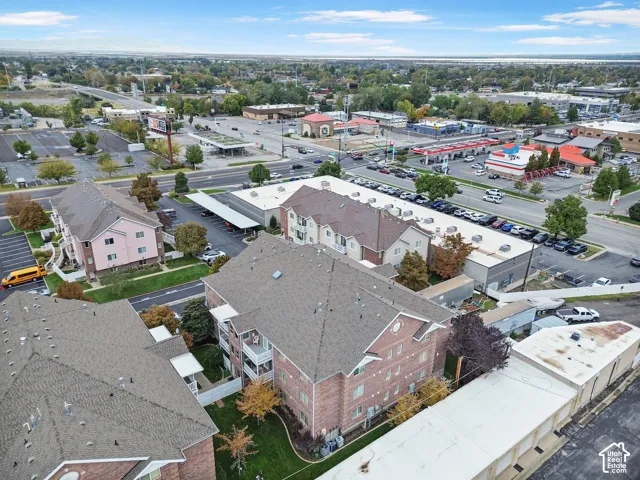 Multi-story brick building featuring pitched shingle roofing, private balconies, and surrounding green space with asphalt parking areas