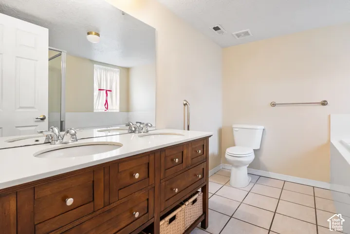 Bathroom featuring a double vanity with wood-finish cabinetry, a white countertop with dual undermount sinks, a full-width wall mirror, and tiled flooring