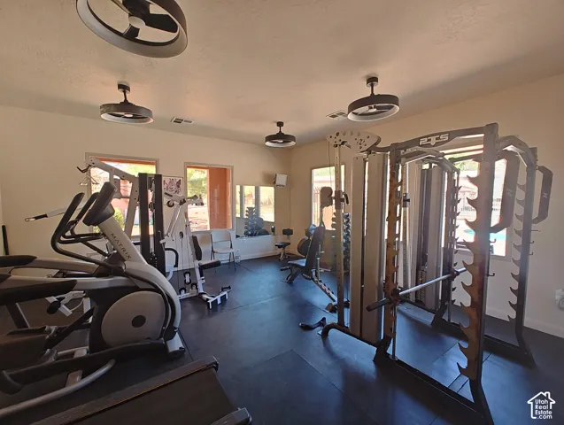 Spacious room featuring resilient rubber flooring, multiple dual-purpose ceiling fan and light fixtures, and windows with natural light exposure