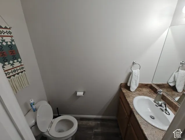 Bathroom featuring a wood-finish vanity with a stone-composite countertop, oval undermount sink, chrome faucet, and wood-finish flooring