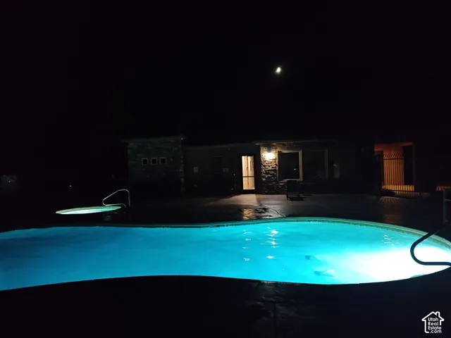 In-ground swimming pool and hot tub with stone-accented exterior, stamped concrete patio, and metal perimeter fencing