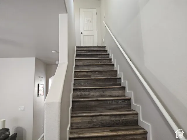 Staircase featuring wood-finish treads, white handrail, and white interior door with a two-panel design