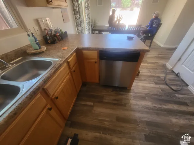 Kitchen featuring wood-finish cabinetry, laminate countertops, a dual-basin stainless steel sink, and wood-finish flooring