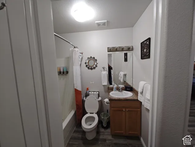 Bathroom featuring a wood-finish vanity with a stone-composite countertop, integrated sink, and an attached four-light fixture above a wall-mounted mirror, alongside a combination tub and shower enclosure with wood-finish flooring
